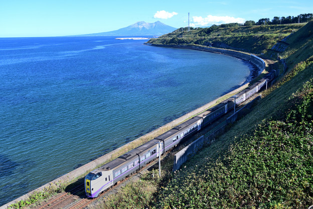 写真: 海岸線のカーブを行く特急列車